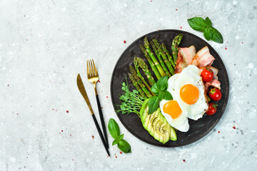 Breakfast. Scrambled eggs, asparagus, bacon and avocado. On a black stone plate.