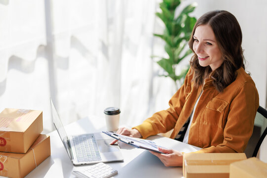 Concept of parcel delivery and selling online, Female seller or retailer using laptop to check sales of the day on online store to be packed into the parcel and ready to deliver to the customer