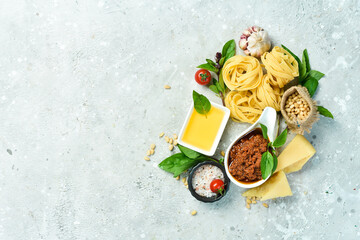 Cooking background: pesto sauce, pasta, basil, parmesan and nuts, olive oil. On a concrete background.