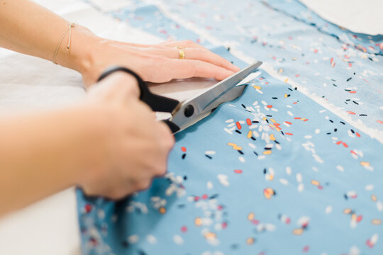 Unrecognizable designer cutting fabric in atelier