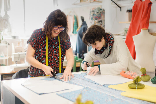 Focused women cutting fabric in atelier