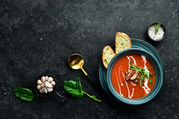 Fototapeta na wymiar Tomato soup with bacon, onion and cream. Mexican cuisine. On a black stone background.