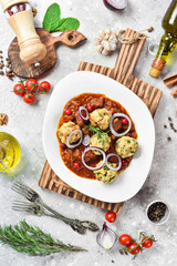 Veal baked in tomato sauce with meatballs. On a white plate. On a gray stone background. Restaurant menu.