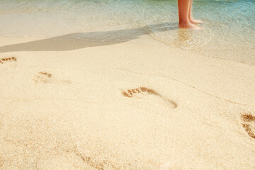 A Beach travel - woman relaxing walking on a sandy beach leaving footprints in the sand. Close up detail of female feet on golden sand at a beach in Greece. Background.