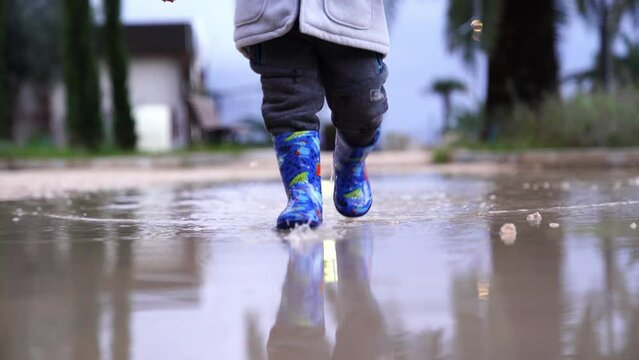 Little girl in a jacket and rubber boots runs through the puddles
