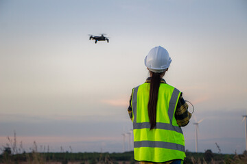 asian female engineer using drone for  inspection wind turbine farm in evening.