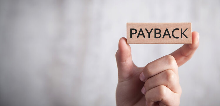 Human hand showing Payback word on wooden block.