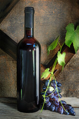 Bottle with red wine and branch grape on wooden table against old canvas background