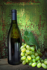 Bottle with white wine and branch grape on background of wooden wall with texture of old paint