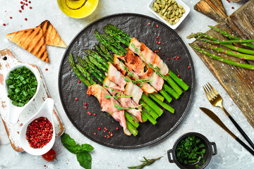 Grilled asparagus with bacon and basil on a plate. On a stone background. Top view.