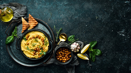 Hummus with chickpeas and rosemary in a black stone plate. Vegetarian food. Top view. On a black stone background. - obrazy, fototapety, plakaty