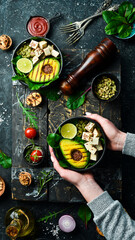 Female hands holding a bowl of vegan lunch: avocado, tofu cheese, flax, pumpkin seeds and spinach. The concept of healthy eating. Top view.