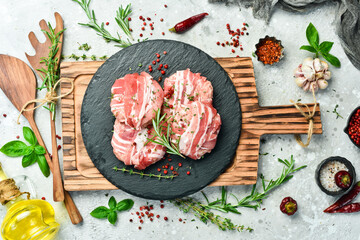 Raw cutlets in bacon served on a black plate with rosemary and thyme. On a gray background. Top view.