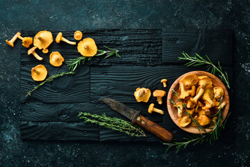 Organic wild chanterelle mushrooms in a bowl. On a black stone background. Top view. - obrazy, fototapety, plakaty