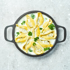 Pasta stuffed with meat, cream sauce and parmesan. In a frying pan. Traditional Italian lunch. On a stone background. Recipe.