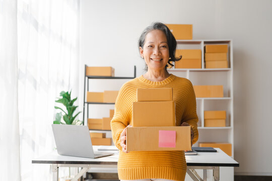 Asian elderly older female mature woman fashion designer sme business owner with product package box at warehouse, merchant seller checking customer address order confirming parcel delivery.