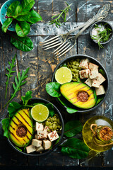 Healthy dinner or lunch. Vegetarian food in a bowl: avocado, tofu cheese, flax, pumpkin seeds and spinach. The concept of healthy eating. On a black stone background. Top view.
