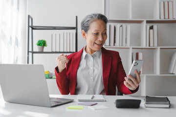 Asian elderly older female mature business woman in formal suit stock trader on stock market and money exchange rate trading working in modern office workplace.