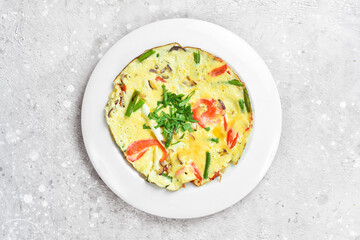 Breakfast. Omelette with cheese and vegetables. On a white plate. On a gray stone background. Restaurant menu.