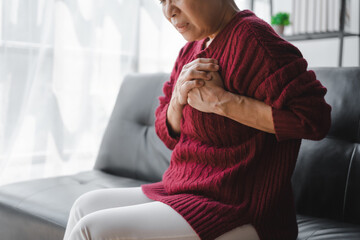 Elderly asian housewife woman sitting on sofa. Heart disease, chest pain, irregular heartbeat