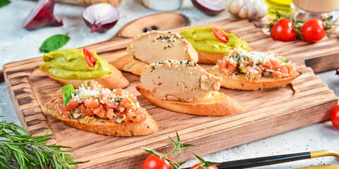 Set bruschetta. Sandwiches with avocado, liver pâté and vegetables. On a white plate. On a gray stone background. Restaurant menu.
