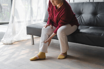Elderly asian housewife woman sitting on sofa. calf pain © Phushutter