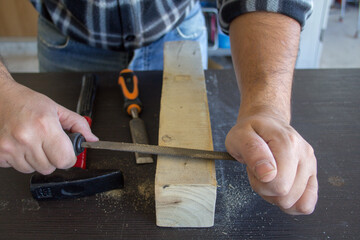 Image of the hands of a carpenter craftsman who smoothes a piece of wood with a rasp. Wood filing...