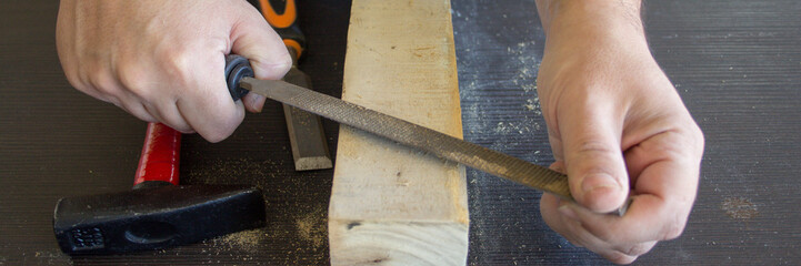 Image of the hands of a carpenter craftsman who smoothes a piece of wood with a rasp. Wood filing and cleaning. Horizontal banner 
