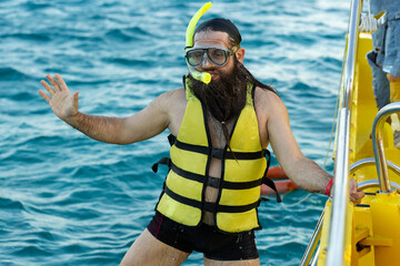 A bearded man diver in a life jacket climbs on board a boat in the sea.