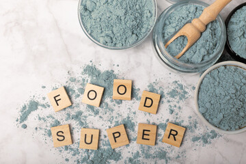 Fototapeta na wymiar Blue spirulina powder in jars, bowls and spoons on a marble background. Natural superfood, vegan, healthy food supplement. Phycocyanin extract. Antioxidant. Place for text. Copy space.
