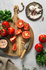 Tomatoes on a wooden cutting board, in different shapes, some halved, some quartered, with fresh...