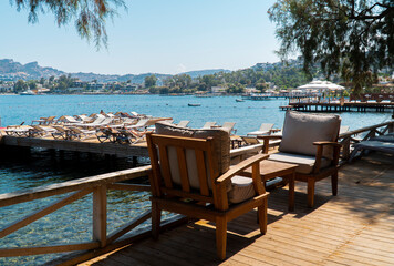 Beach club view with  wooden tables, chairs and sun loungers in the background by the sea Bodrum,...