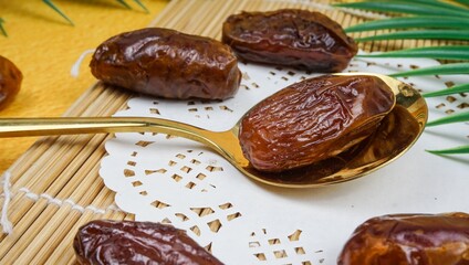 Kurma or dried dates in a golden spoon over yellow background. Popular during Ramadan for fasting energy.