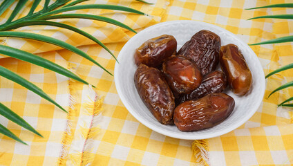Pile of sweet dried dates in white plate, againts yellow napkin