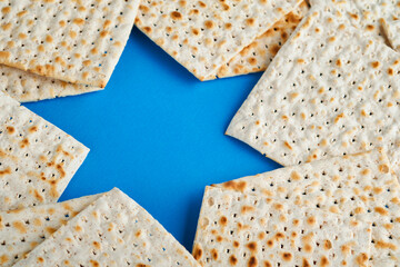 Passover celebration concept. Blue Star of David made from matzah, white and yellow roses, kippah and walnut on bluebackground. Traditional ritual Jewish Passover food. Pesach Jewish holiday. Mock up