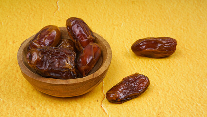 date fruit or kurma in wooden bowl isolated on yellow background