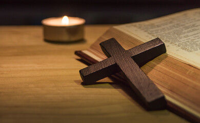 cross and bible with a lit candle on the background
