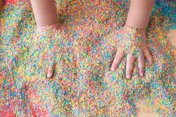 Two hands mixing colourful sensory bin