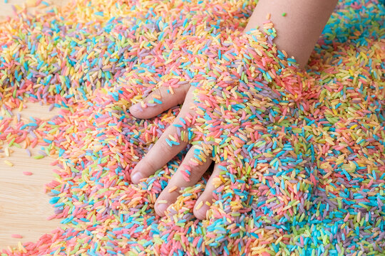 Two hands mixing colourful sensory bin