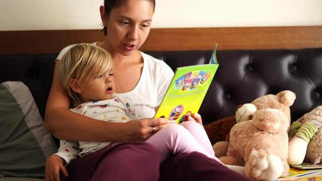 Mom reads a picture book to a little girl on the bed
