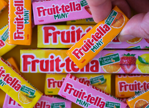 Tambov, Russian Federation - January 22, 2023 A woman hand holding orange Fruit-tella mini candy against a pile of Fruit-tella candies packs with different flavoured.