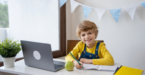 Caucasian smiling child schoolboy or girl studying at home using laptop remote education. Looking...