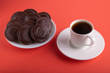 photo round chocolate-covered cookies lying on a plate next to a cup of hot coffee