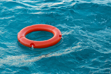 A red lifebuoy floats on the waves of the turquoise sea.
