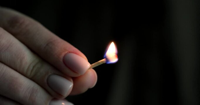 Woman hand holds burning match on black background