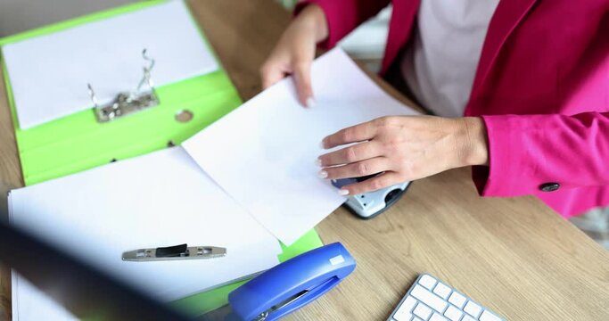 Closeup of female hands making holes with paper on documents on office table