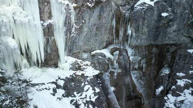 the stuiben falls in the mountains near the town of reutte in austria with trees and mountains covered with snow. the waterfall is slightly frozen taken with a drone