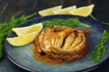 sprat fish in tomato sauce on the plate with lemon slices and dill closeup photo