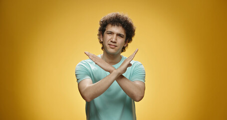 Guy gesturing no. Young asian man with curly hair in casual clothing looking at camera and gesturing bo with arms crossed, isolated on yellow background close up 