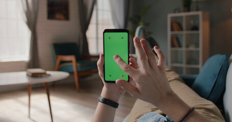 Close up shot of man lying on couch and using smart phone with chroma key green screen, doing various taps, swipes and scrolls - technology, communication 